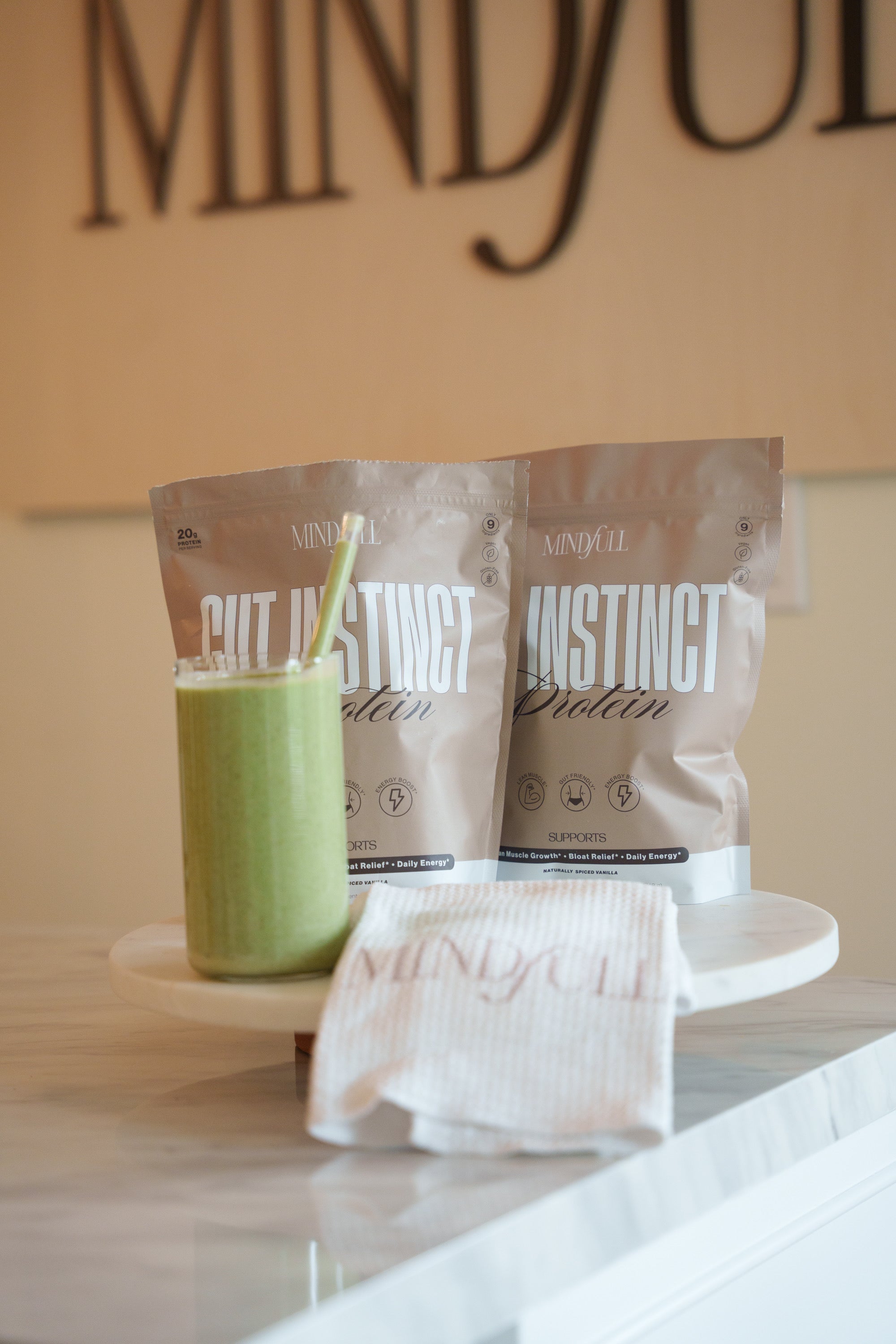 Two protein powder packets and a green smoothie on a white surface with 'MINDFULL' in the background.